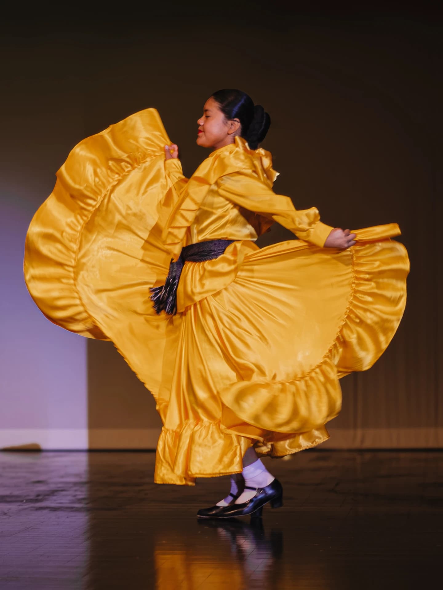 Student performer in a yellow dress on a dark stage